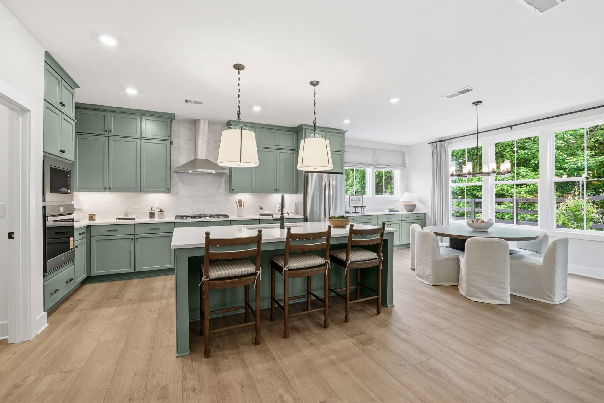 Kitchen with sage green cabinets, an island with seating, and pendant lights